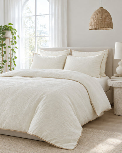 Cream piped cloud cotton bedding set beneath an arched window with a trailing pothos and rattan pendant