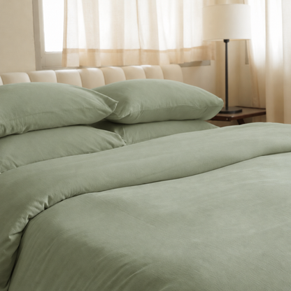 Mint Green plain cotton bedding on a bed with a tufted headboard, sheer curtains and a floor lamp.