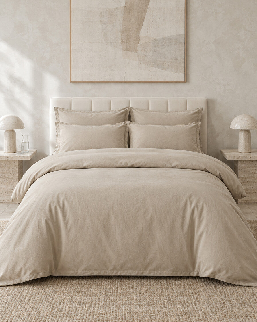 Sand plain cotton bedding set against a limewashed plaster wall between travertine bedside tables