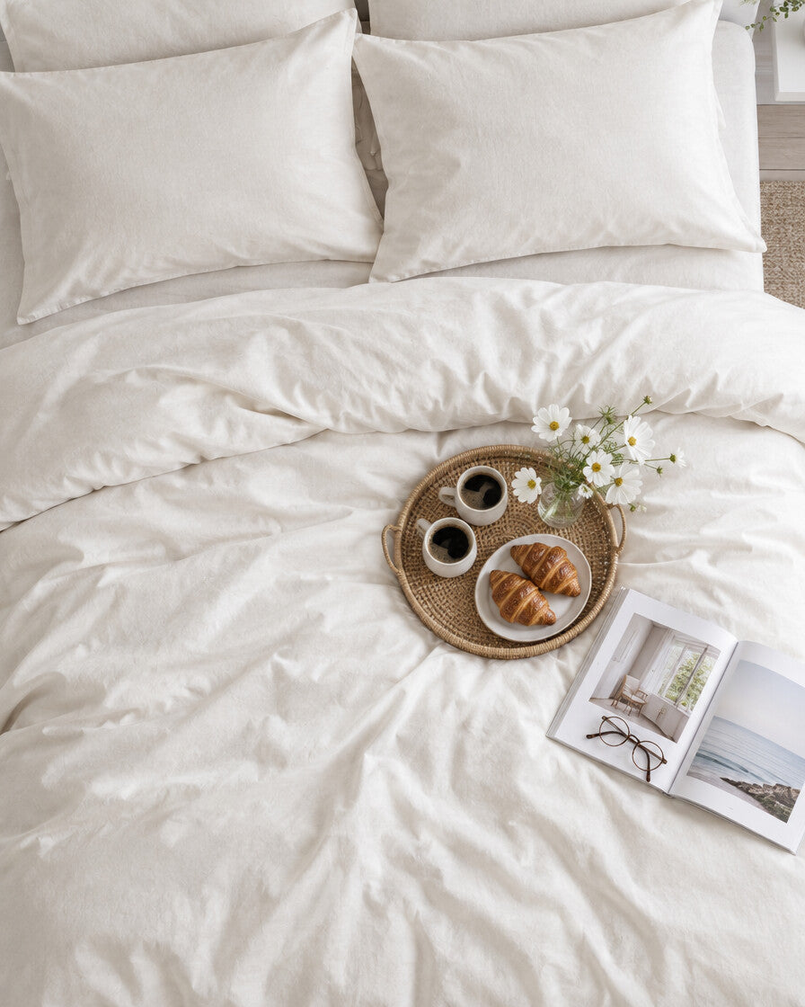 White plain cotton bedding set seen from above with a breakfast tray of coffee and croissants