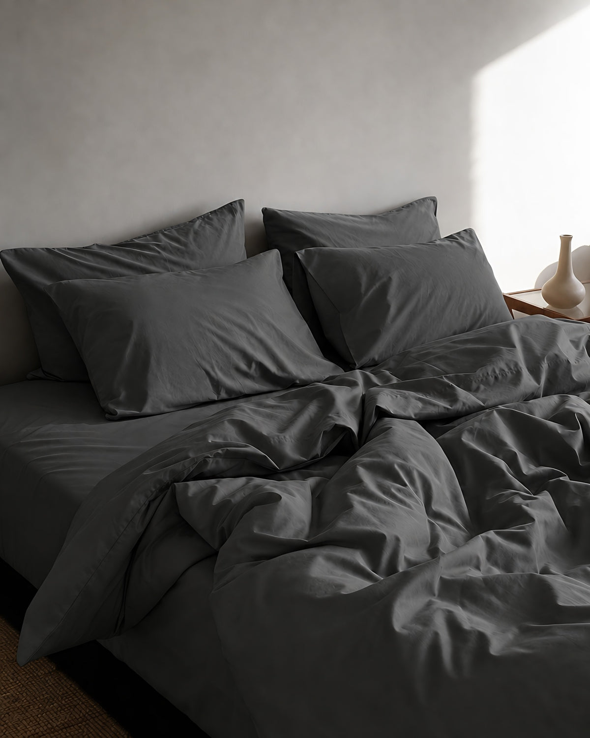 Charcoal Grey silky cotton duvet cover, pillowcases and sheet, softly rumpled on a bed in afternoon window light