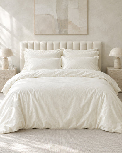 Ivory silky cotton bedding set against a limewashed plaster wall between travertine bedside tables