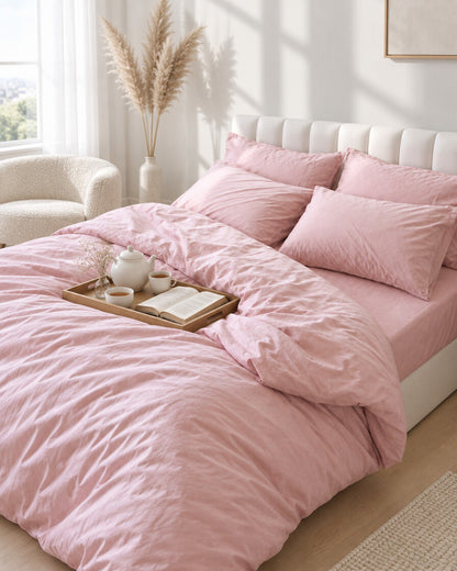 Blush pink silky cotton bedding set with a tea tray and open book, a boucle armchair in the corner