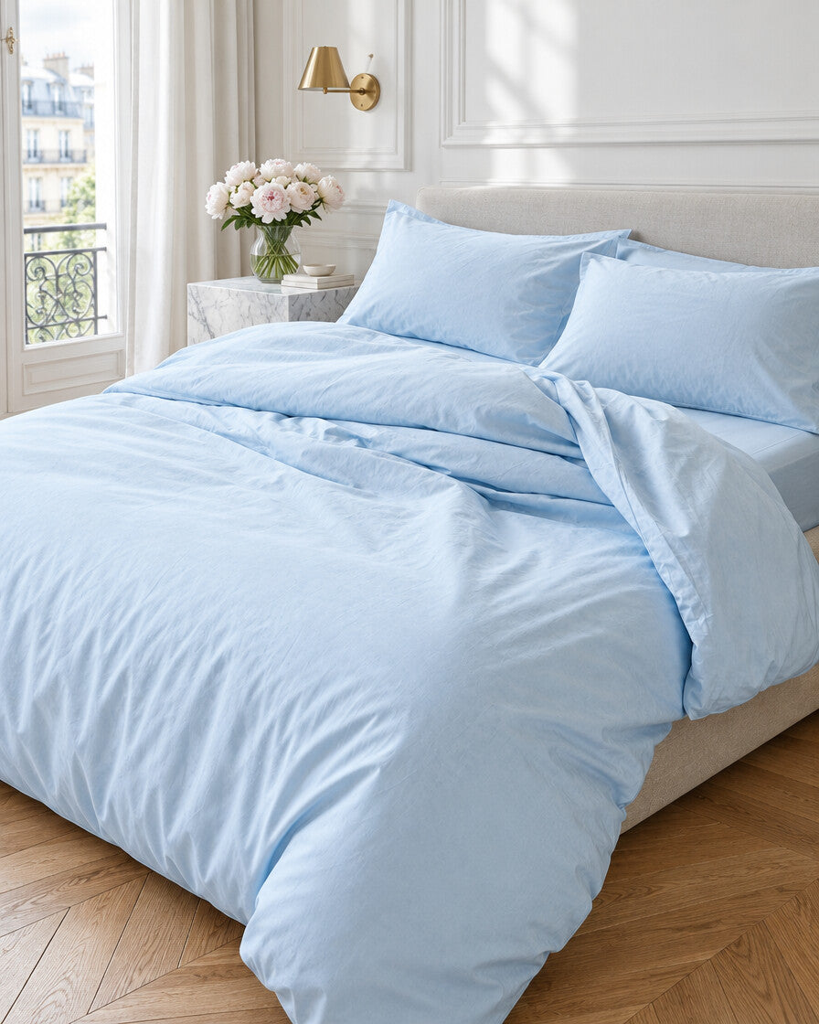 Pale blue silky cotton bedding set in a Parisian bedroom with panelled walls and fresh peonies