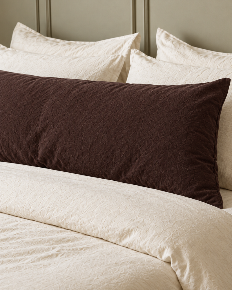 Chocolate plain cotton body pillowcase in rich dark brown on a long pillow before cream pillows