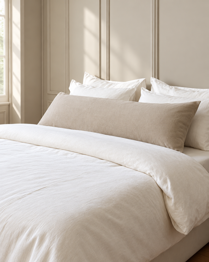 Beige plain cotton body pillowcase on a long bolster pillow across a white bed in a panelled bedroom