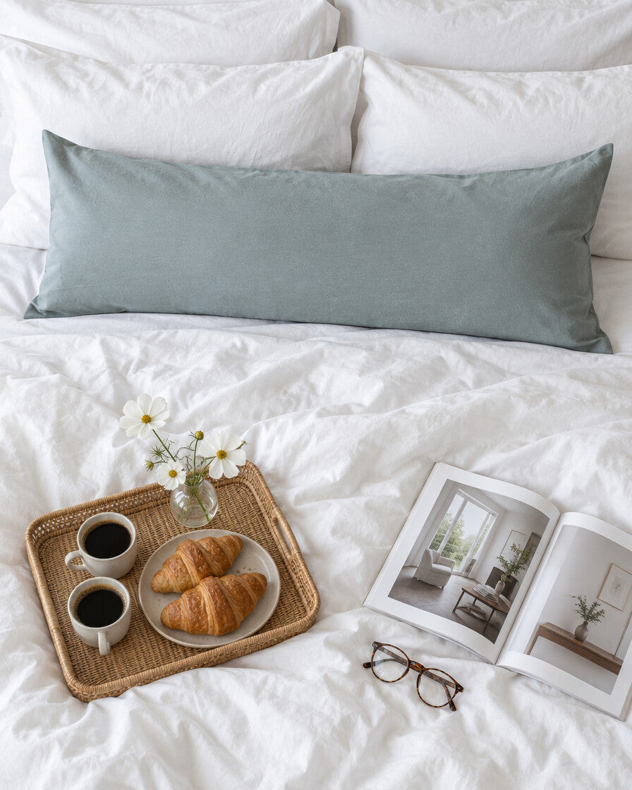 Blue-grey plain cotton body pillowcase seen from above with a breakfast tray of coffee and croissants