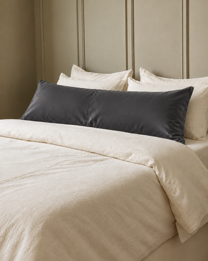 Charcoal Grey silky cotton body pillowcase, a grey cotton sateen body pillow cover, in front of cream pillows on a made bed.