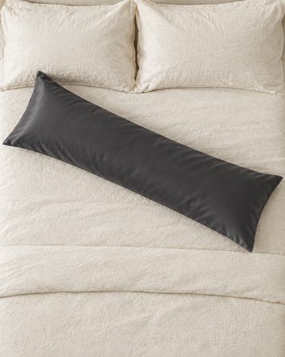 Overhead view of a Charcoal Grey body pillow in a grey silky cotton sateen pillowcase lying across a cream bed.