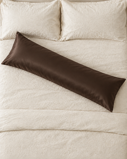 Overhead view of a Chocolate body pillow in a chocolate brown silky cotton sateen pillowcase lying across a cream bed.