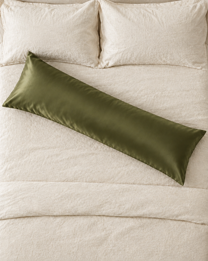 Overhead view of a Juniper Green body pillow in an olive green silky cotton sateen pillowcase lying across a cream bed.