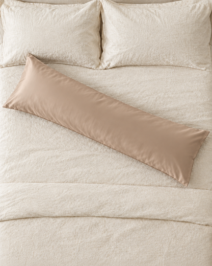 Overhead view of a Light Beige body pillow in a beige silky cotton sateen pillowcase lying across a cream bed.