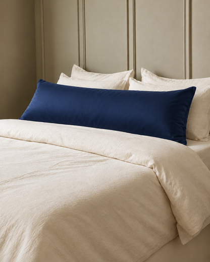 Marine Blue silky cotton body pillowcase, a navy blue cotton sateen body pillow cover, in front of cream pillows on a made bed.