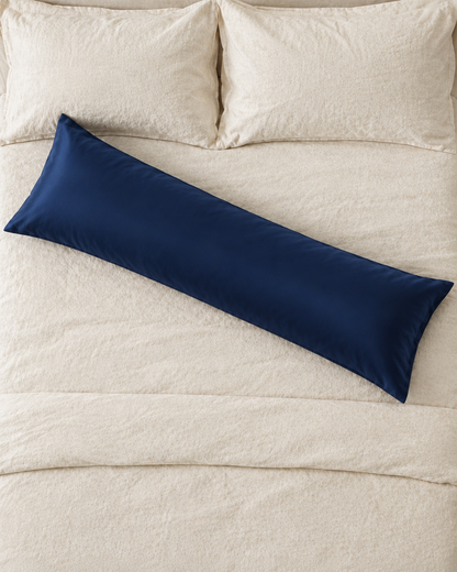 Overhead view of a Marine Blue body pillow in a navy blue silky cotton sateen pillowcase lying across a cream bed.