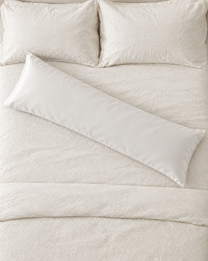 Overhead view of a Milky White body pillow in a white silky cotton sateen pillowcase lying across a cream bed.