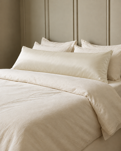 Vanilla silky cotton body pillowcase, a cream cotton sateen body pillow cover, in front of cream pillows on a made bed.