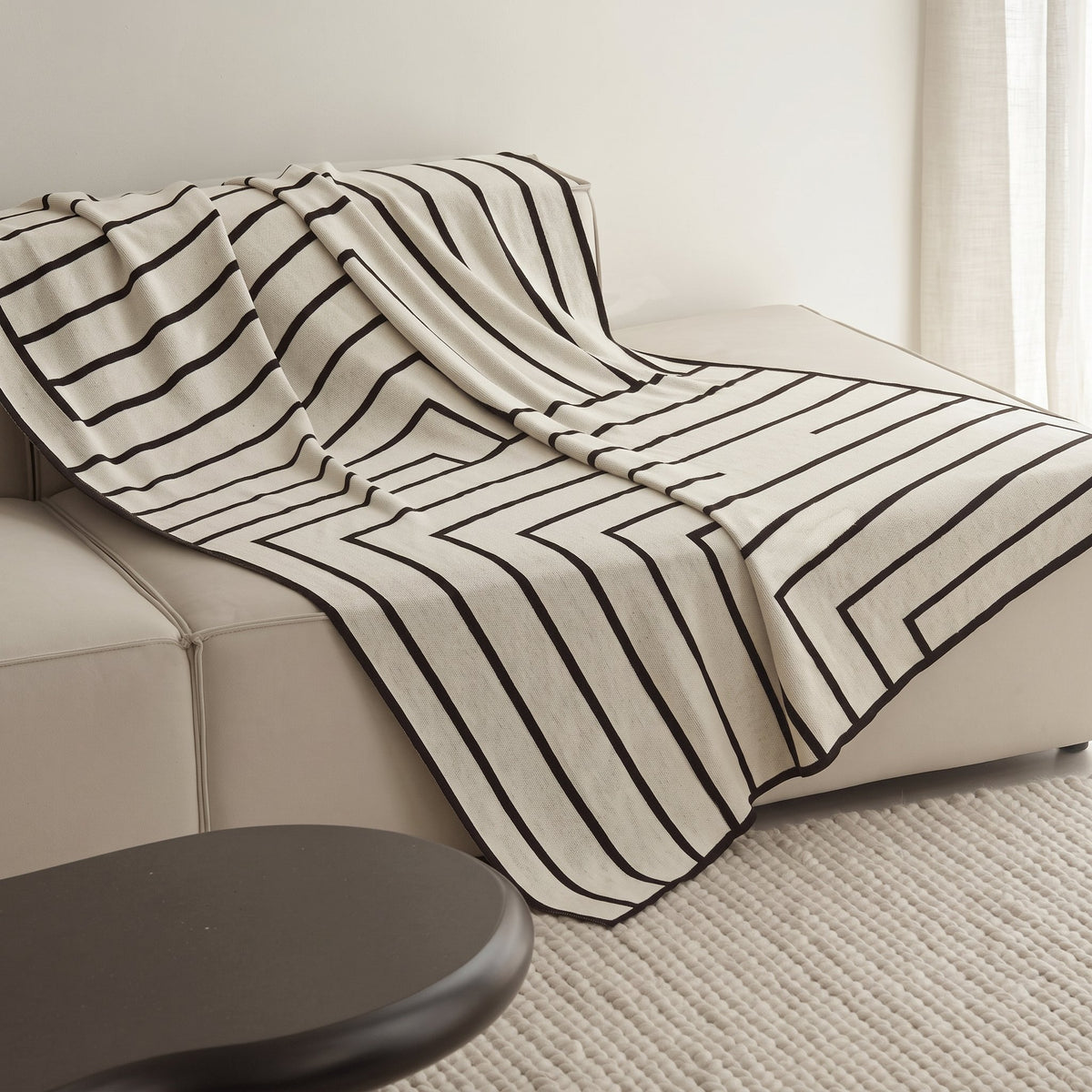 Striped Combed Cotton Knit Throw in ivory and black draped over a cream sofa