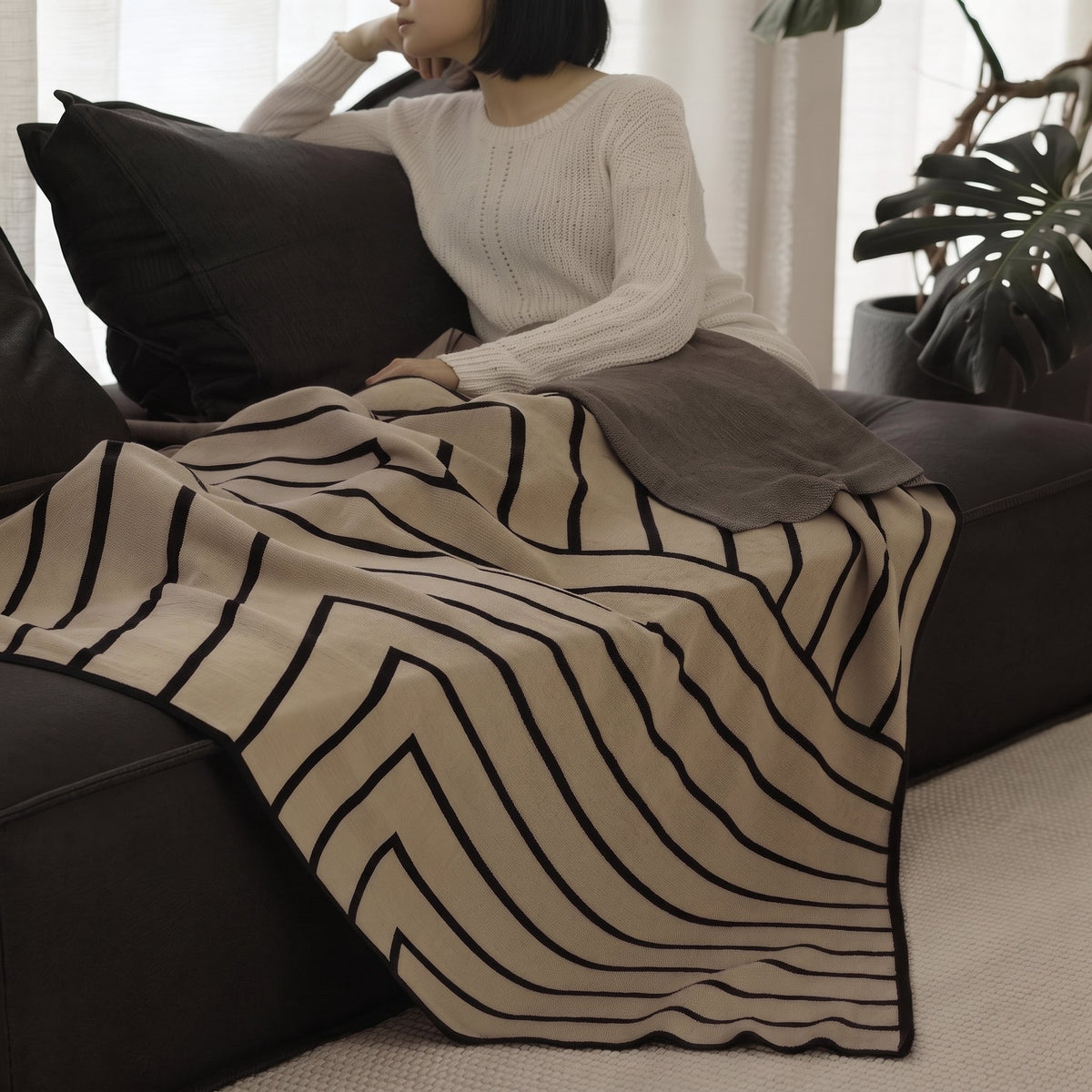 Woman on a dark sofa with the Striped Combed Cotton Knit Throw in taupe and black across her lap