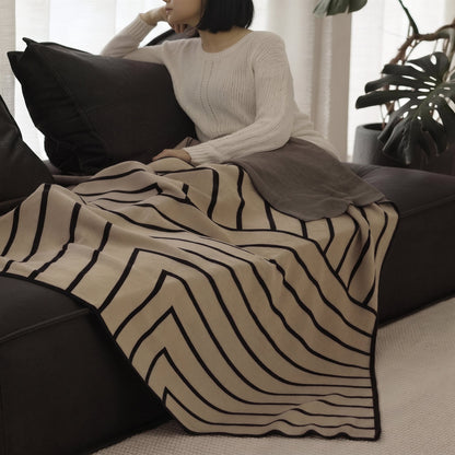 Woman on a dark sofa with the Striped Combed Cotton Knit Throw in taupe and black across her lap