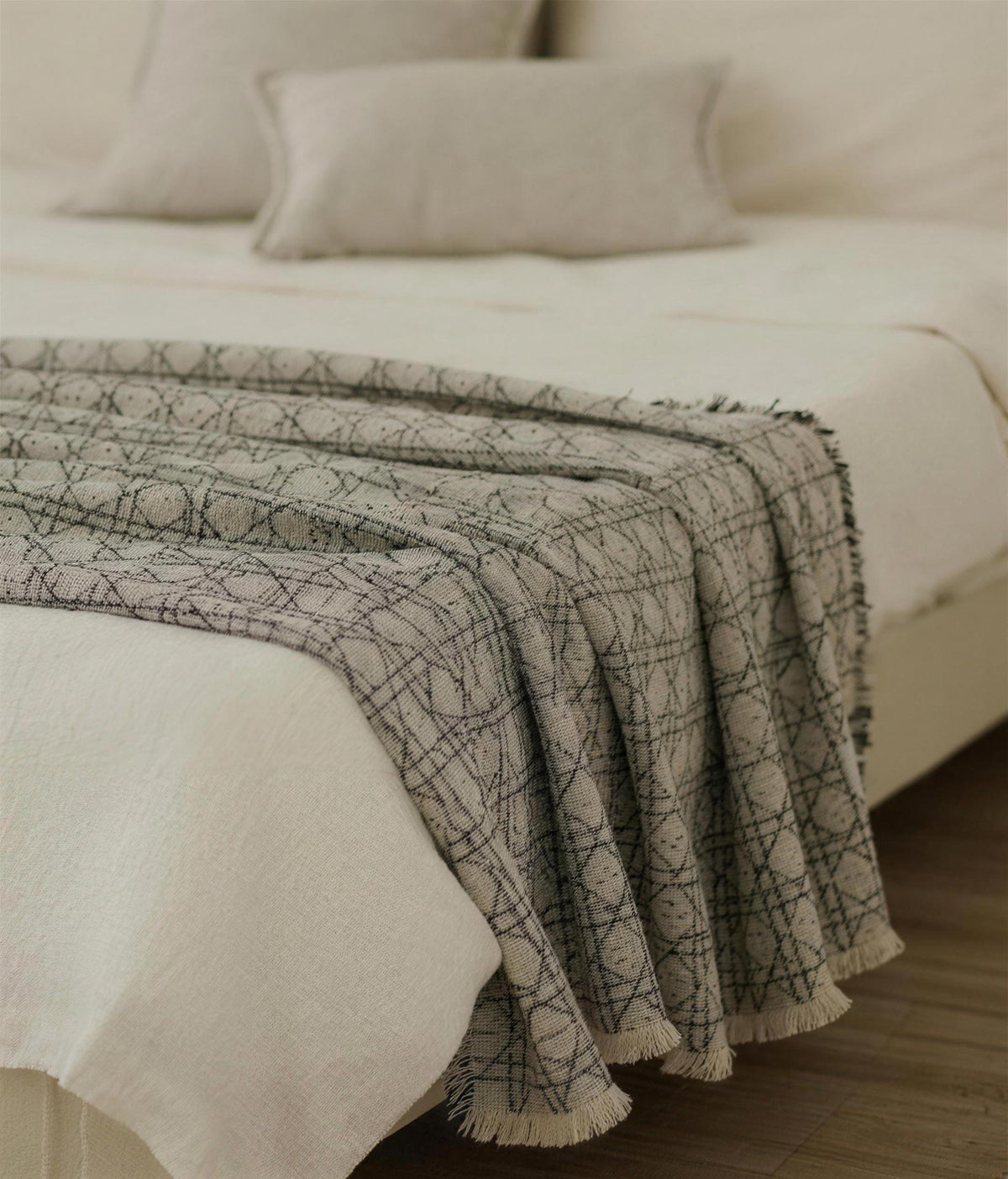 Vine Jacquard throw in Stone and Black draped over the end of a made bed, with fringed edges