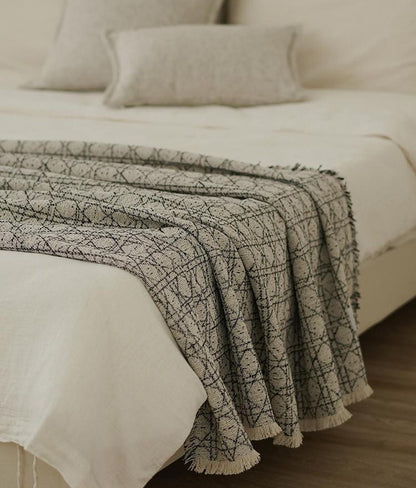 Vine Jacquard throw in Stone and Black draped over the end of a made bed, with fringed edges