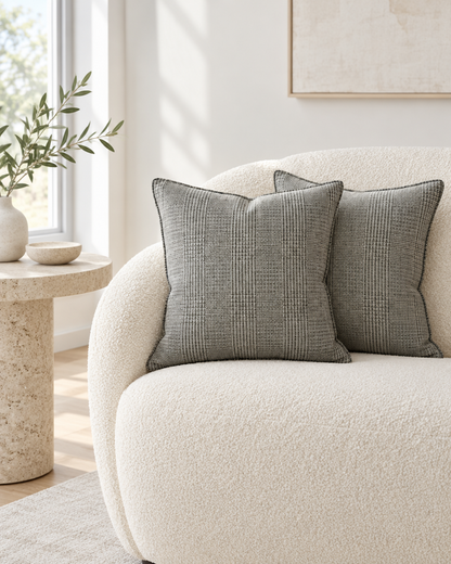 Charcoal fine glen check hemp cotton cushions with dark piping on a cream bouclé armchair beside a travertine table