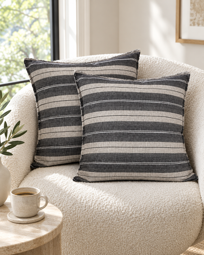 Charcoal and ivory wide stripe linen cushion covers on a curved bouclé armchair by a sunny window