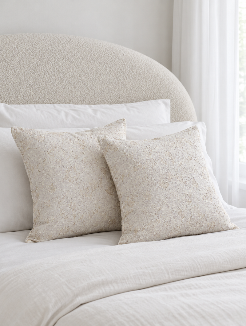 Cream floral jacquard cushions on ivory bedding in front of a curved boucle headboard
