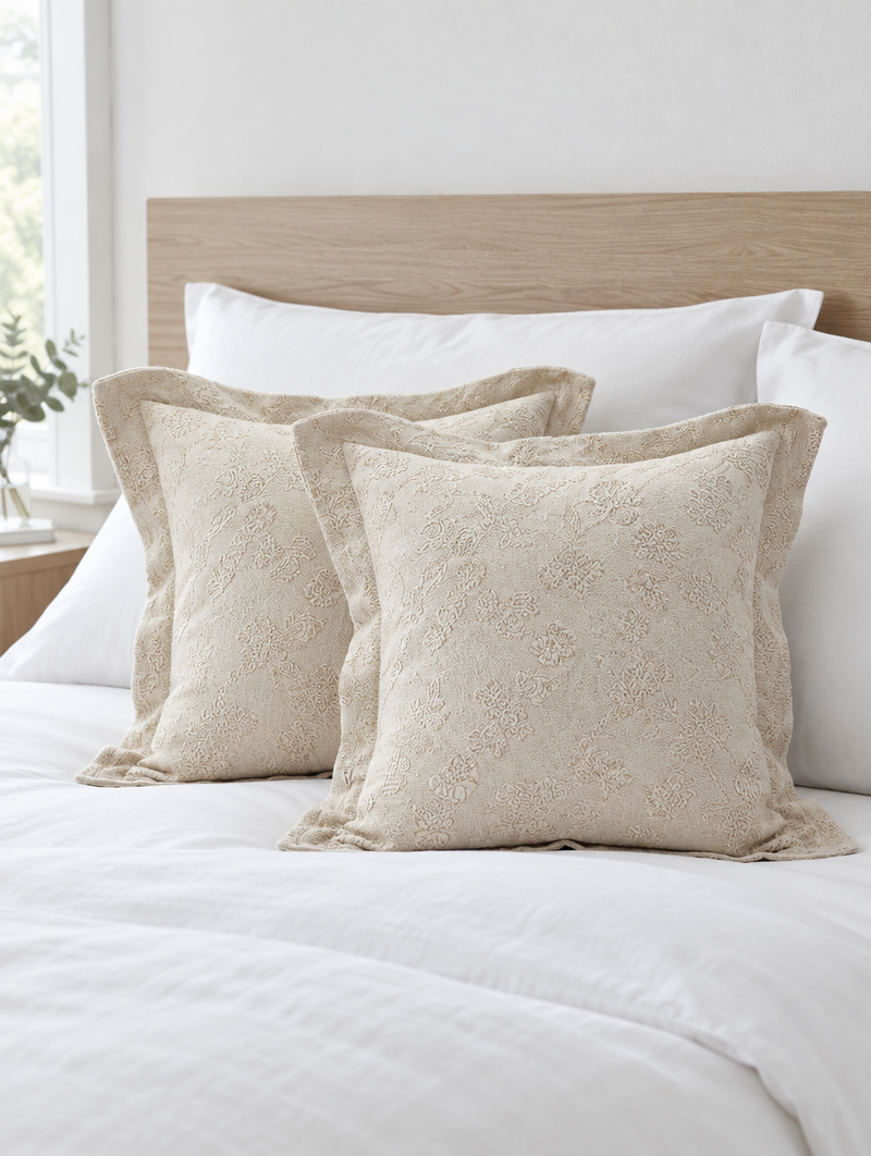 Two cream vine flanged jacquard cushions against a light oak headboard on crisp white bedding