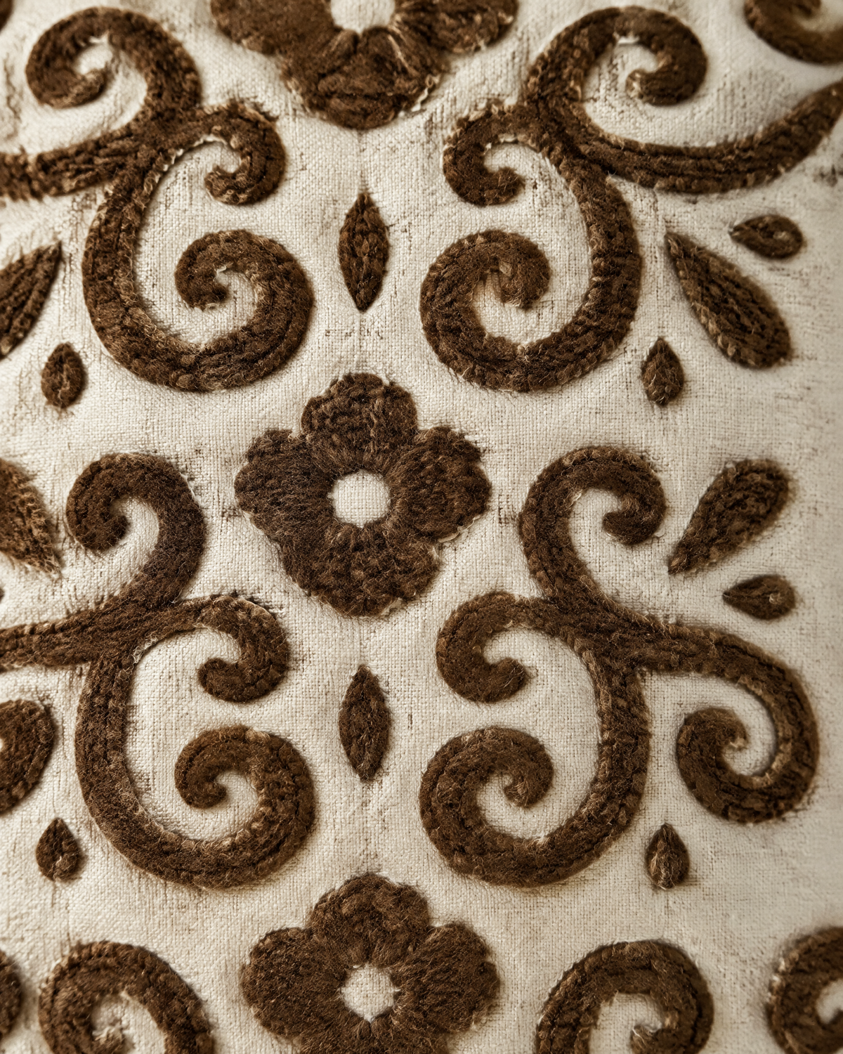 Macro close-up of the ivory and brown embroidery, tufted cocoa scrolls and four-petal flowers on slubbed ivory ramie