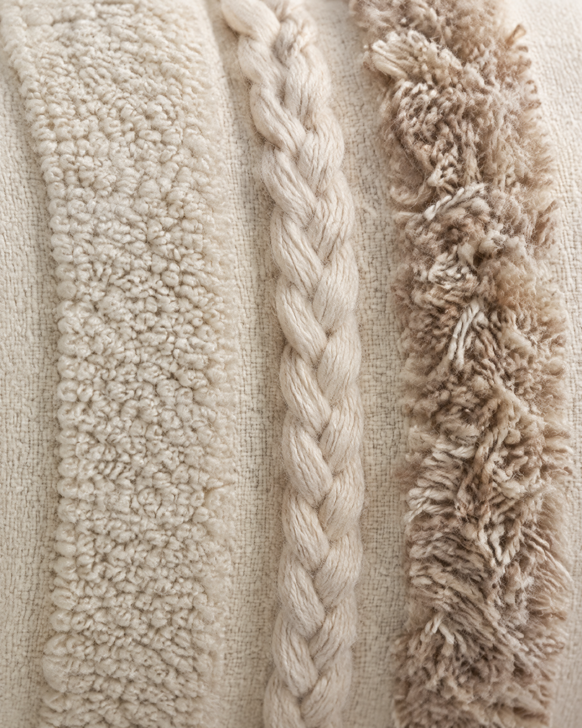 Macro close-up of the ivory and oat banded lumbar, matte loop pile, a braided cord and shaggy oat tufts side by side