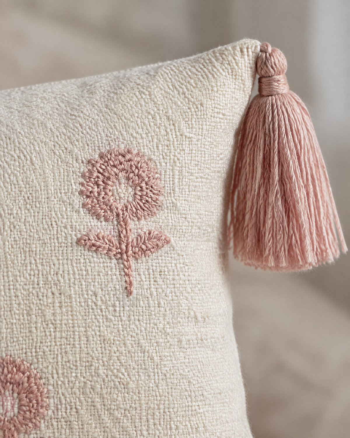Macro close-up of a raised rose-pink flower head and soft pink corner tassel on slubbed ivory ramie