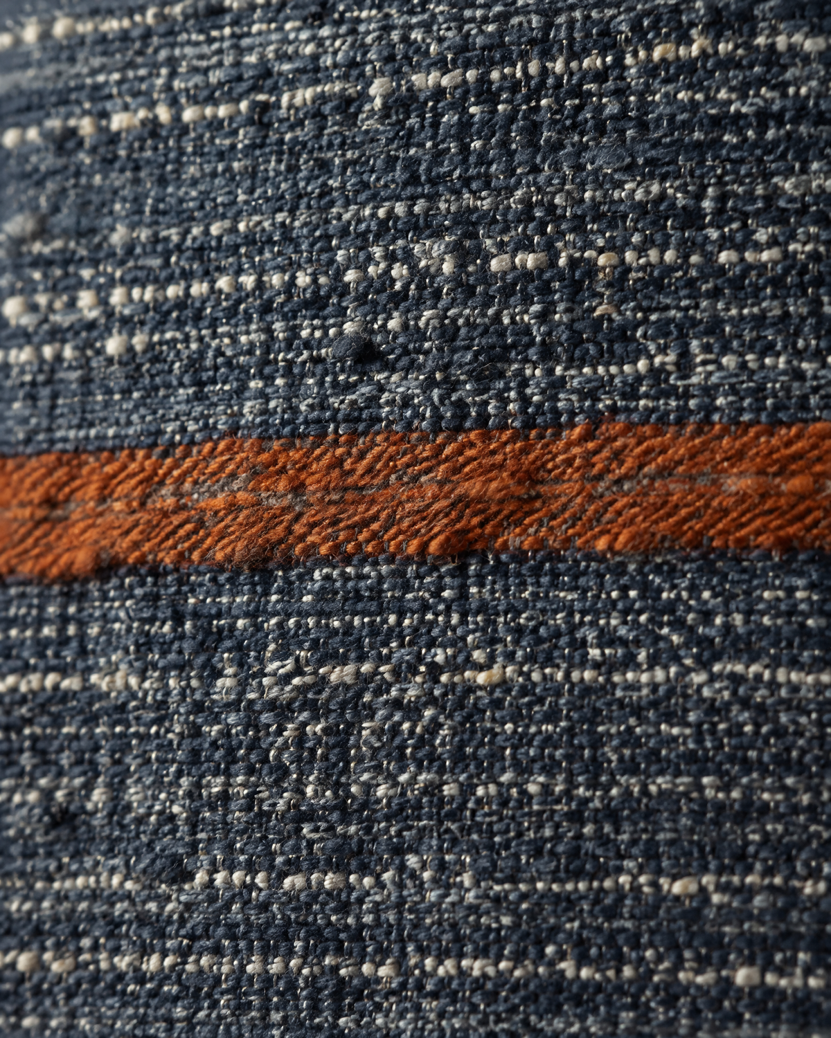 Macro close-up of a slubby rust stripe across heathered navy hemp-cotton weave