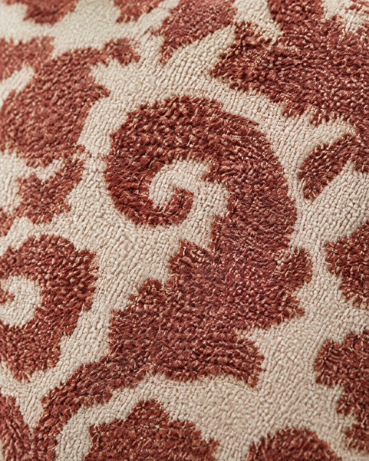 Macro close-up of rust-red damask scrolls in dense raised stitching on a pale cream ground