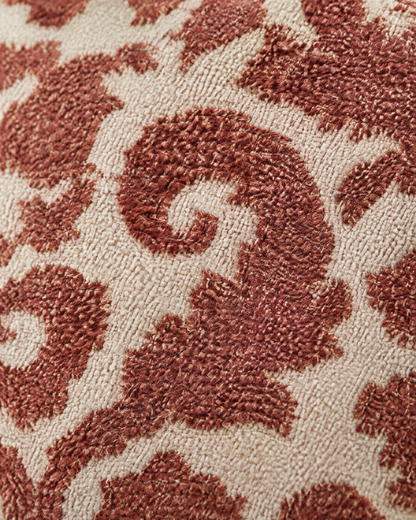 Macro close-up of rust-red damask scrolls in dense raised stitching on a pale cream ground