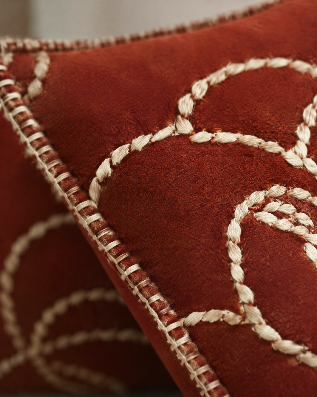 Macro close-up of ivory rope-stitch flower outlines and whipstitched edge on brick-red cloth