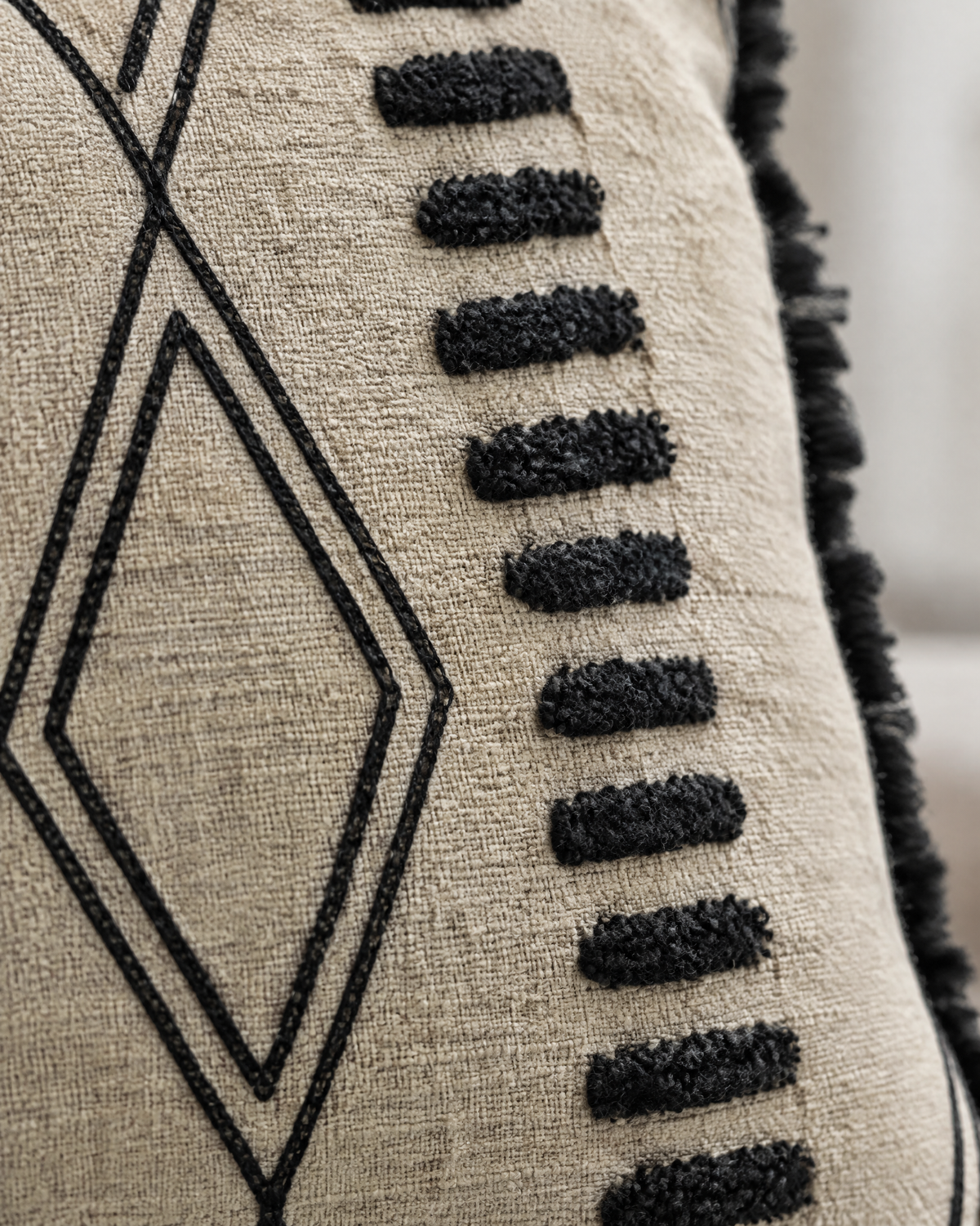 Macro close-up of the sand and black embroidery, tufted black dashes beside chain-stitch diamonds on sand weave
