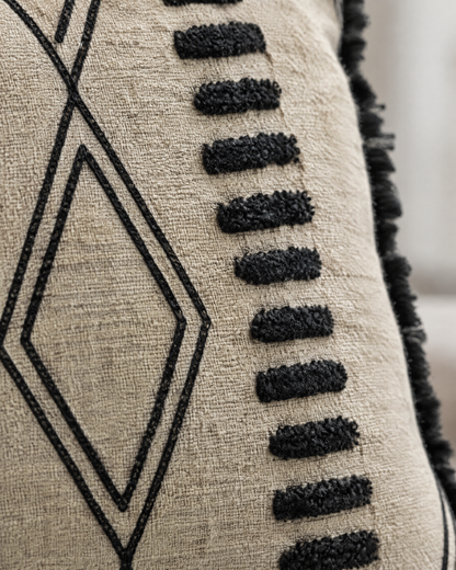 Macro close-up of the sand and black embroidery, tufted black dashes beside chain-stitch diamonds on sand weave
