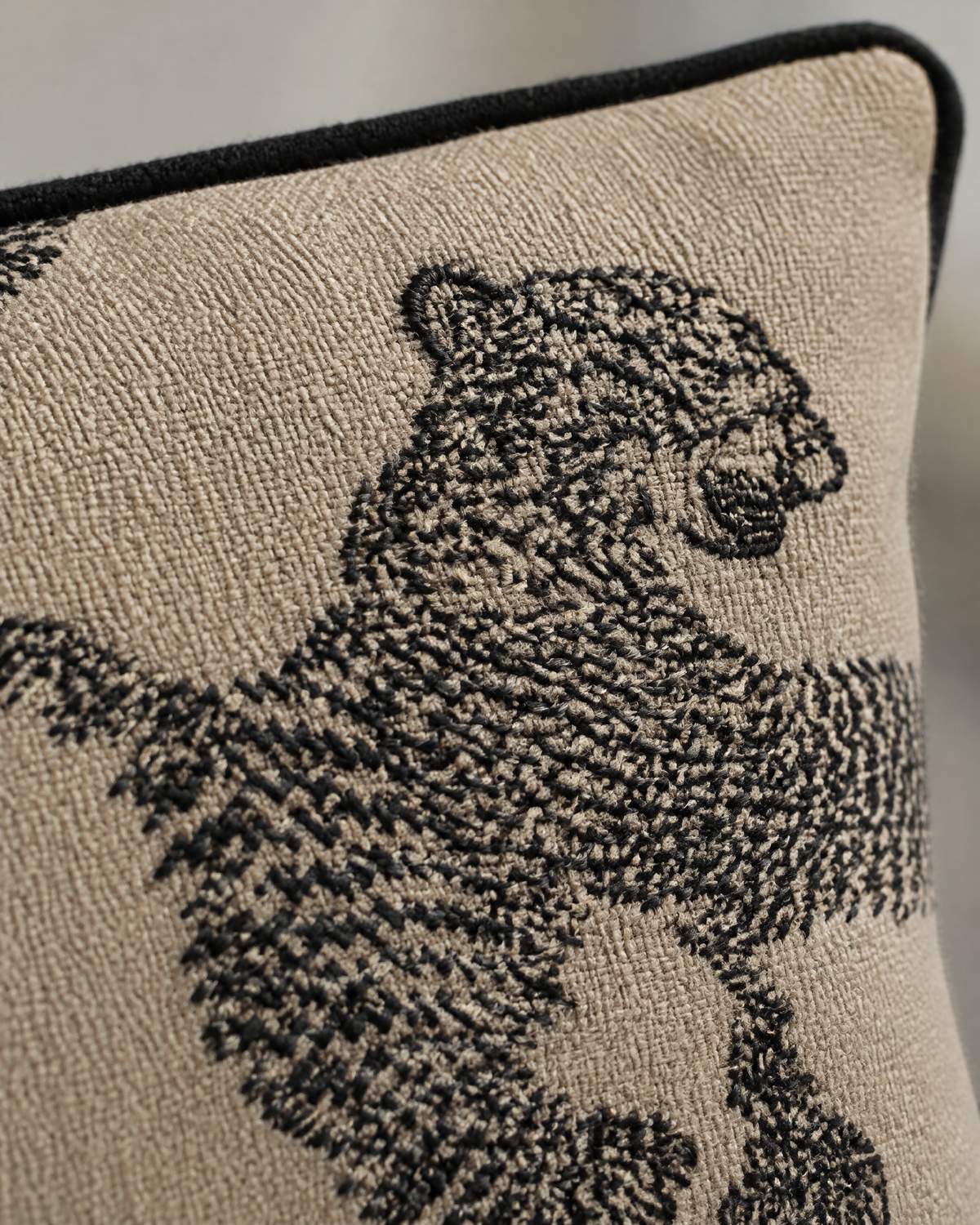 Macro close-up of a black embroidered tiger's head on sand weave below the black piped edge