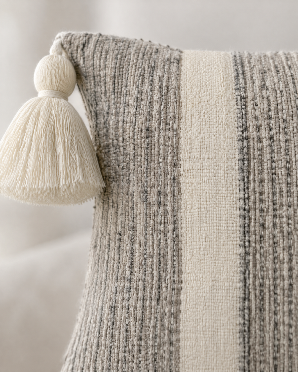 Macro close-up of the stripe tassel cover, ribbed heathered grey cotton beside an ivory band, with a cream tassel