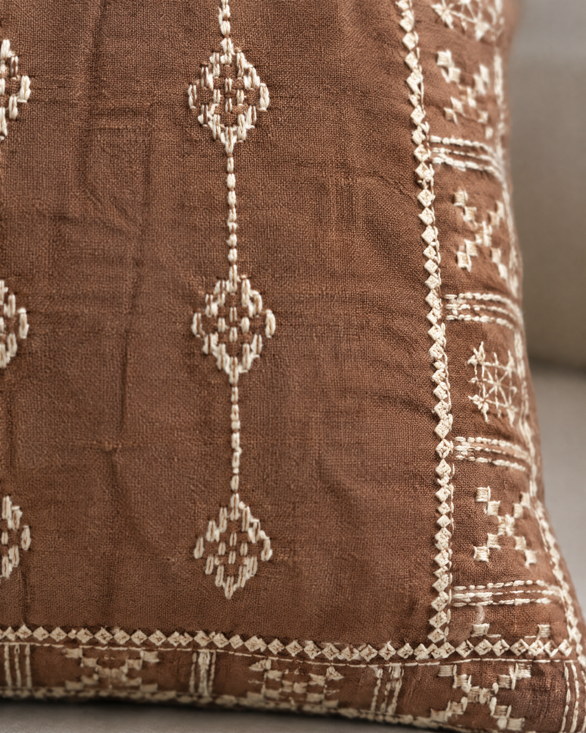 Macro close-up of the terracotta tassel cover, small ivory stitched diamonds and a geometric border on washed terracotta linen cotton