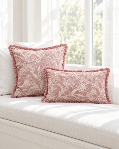 Dusty rose floral print cushions with fringed edges, square and lumbar, on a sunlit white window seat