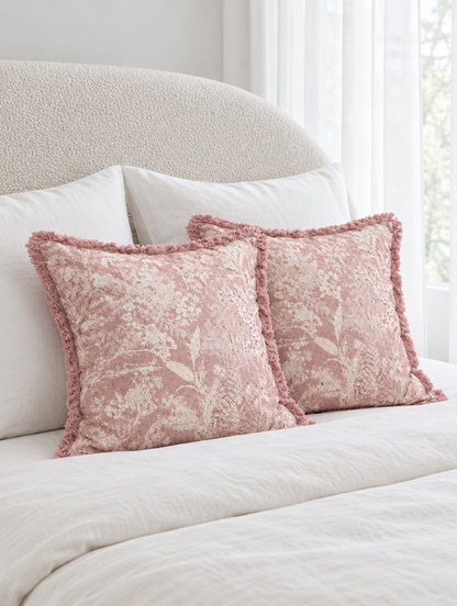 Dusty rose floral cushions with fringed edges on ivory bedding in front of a boucle headboard