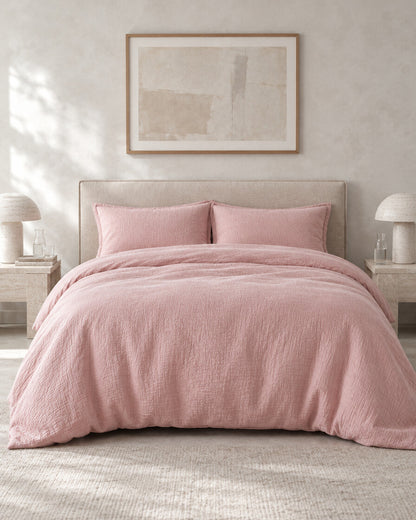 Dusty pink cloud cotton duvet cover against a limewashed plaster wall between travertine bedside tables