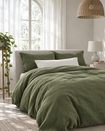 Juniper green cloud cotton duvet cover beneath an arched window with a trailing pothos and rattan pendant