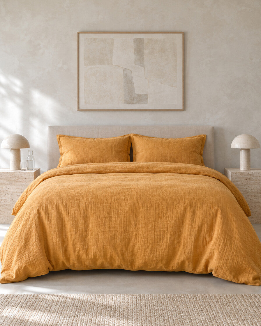 Mustard cloud cotton duvet cover against a limewashed plaster wall between travertine bedside tables