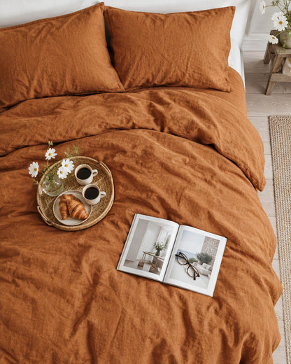 Terracotta French linen duvet cover seen from above with a breakfast tray of coffee and croissants