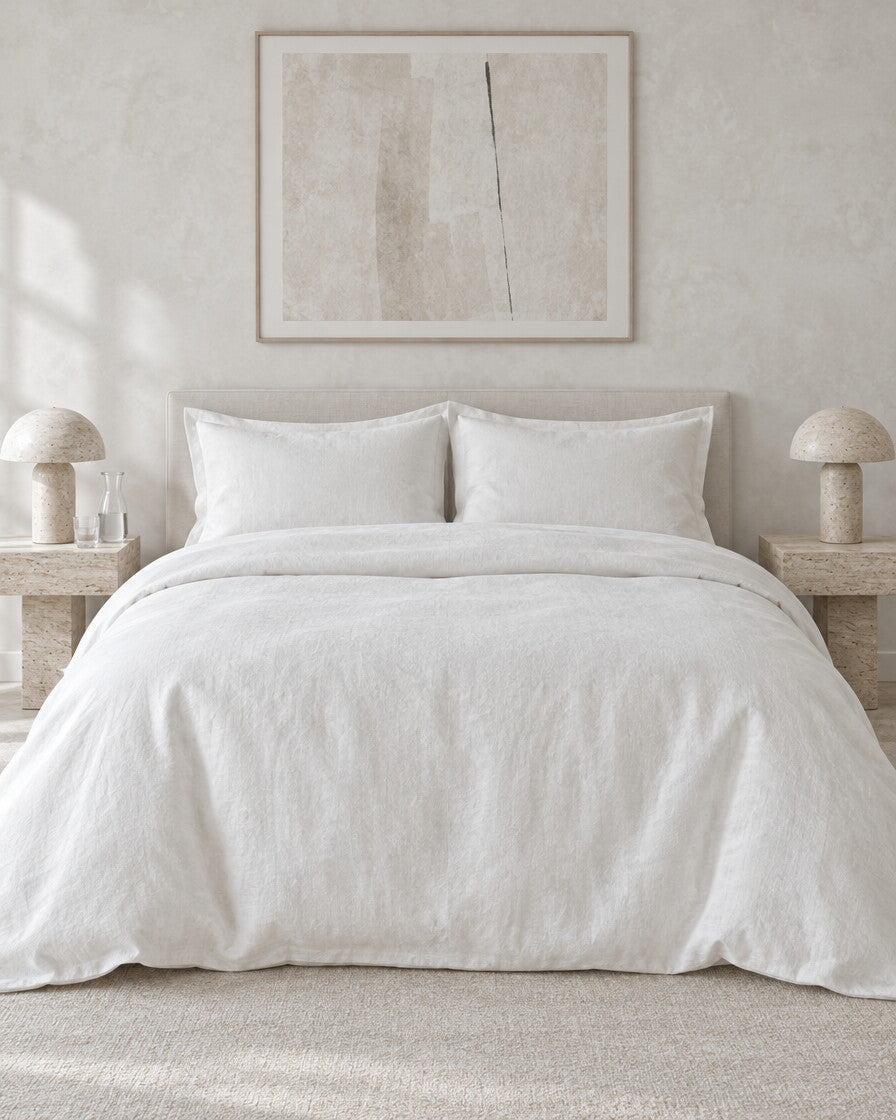 White French linen duvet cover against a limewashed plaster wall between travertine bedside tables