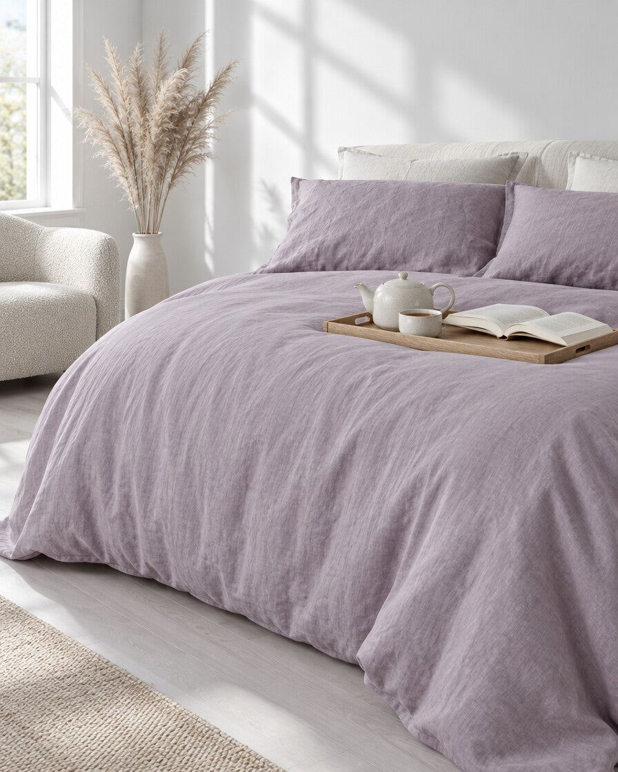 Pale mauve-grey French linen duvet cover with a tea tray and open book, a boucle armchair in the corner