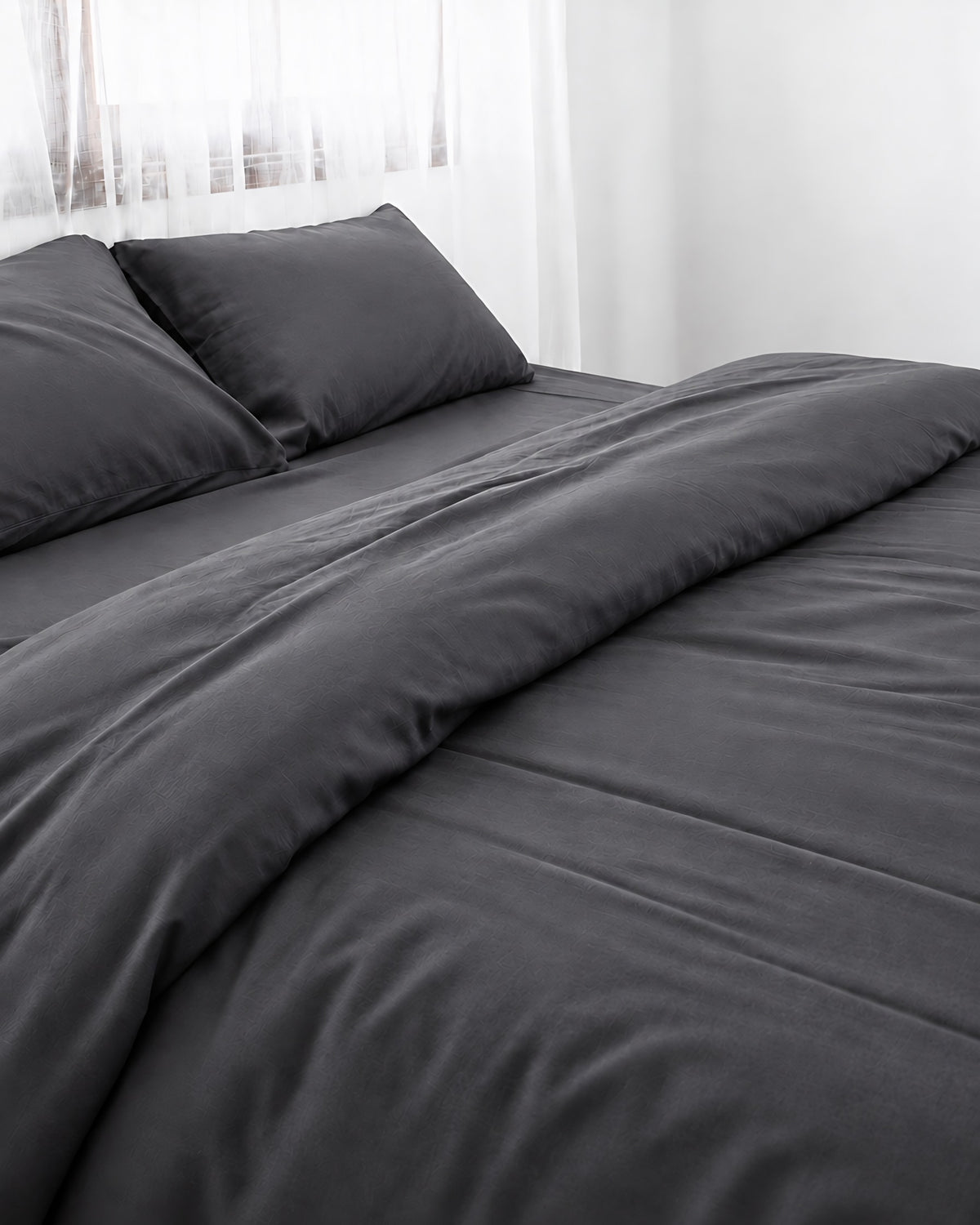 Charcoal Grey silky cotton duvet cover, grey 300 TC cotton sateen, turned back on a bed by a white sheer curtain